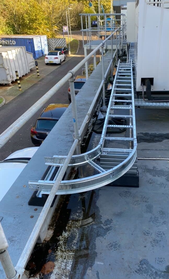 Galvanised cable ladder curving around an external walkway and along the side of a building