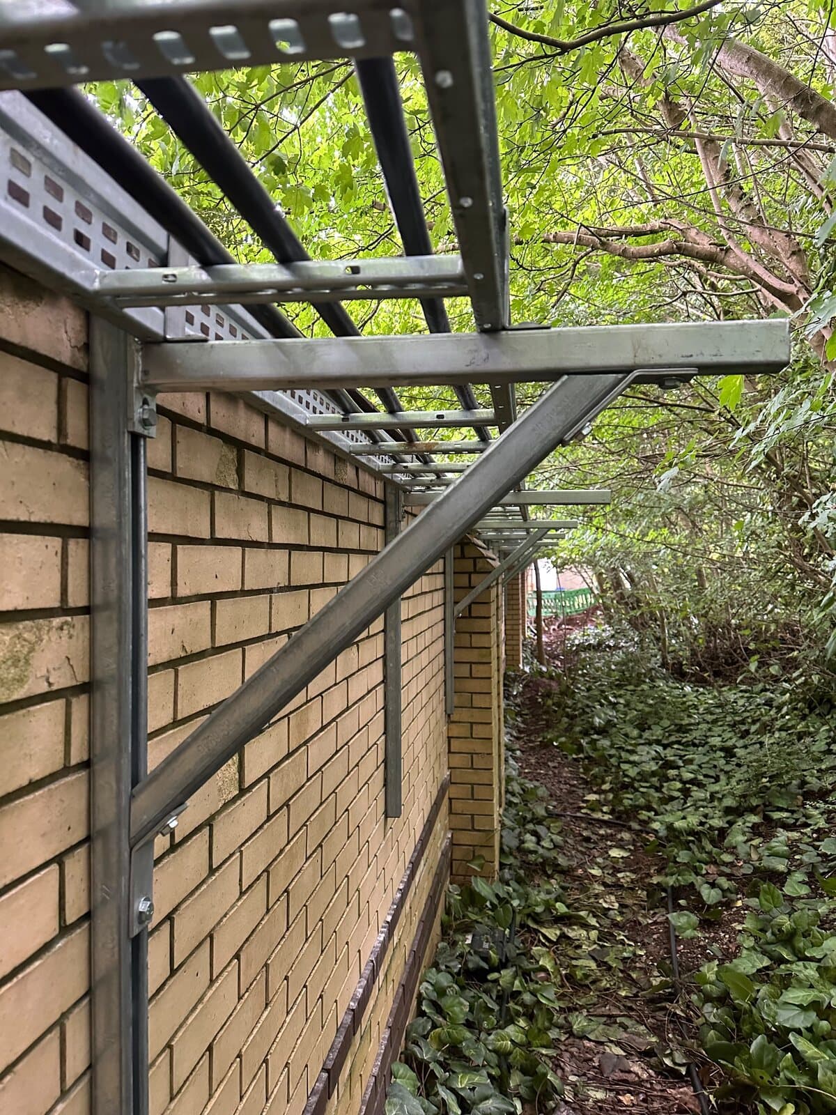 Cable ladder fixed along a brick elevation, brackets set out level the whole run