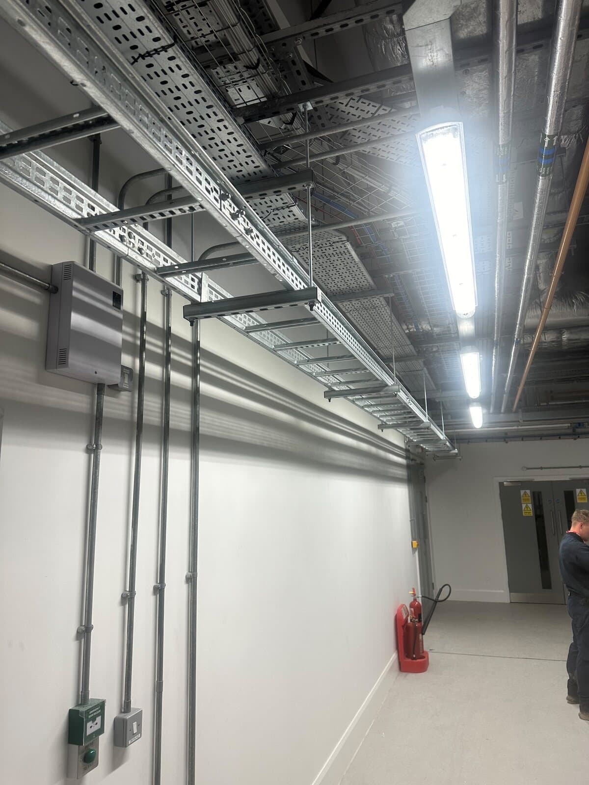 Corridor fitted out with cable tray, conduit drops and LED battens on a newly finished ceiling