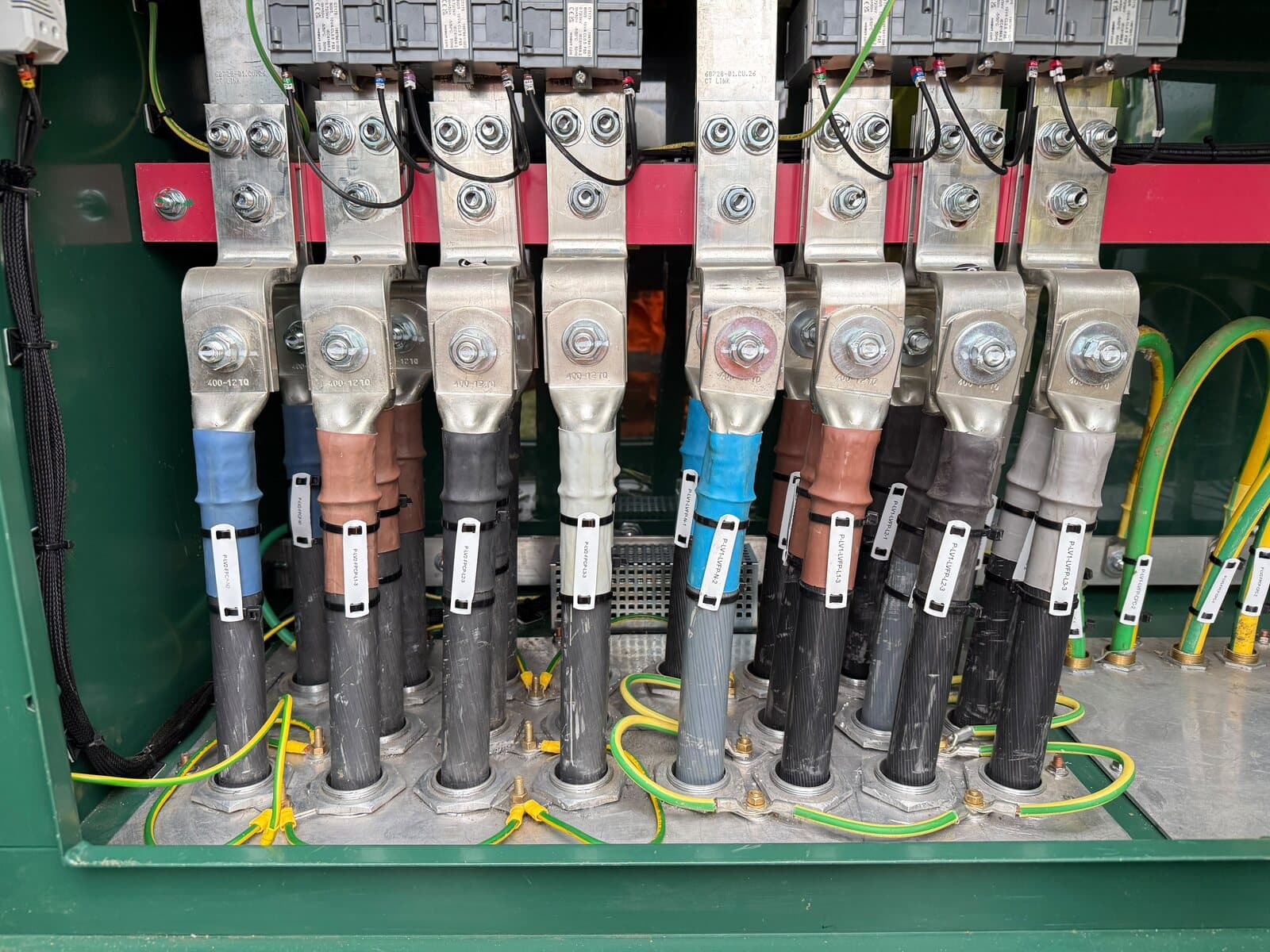 Bank of large armoured cables terminated onto the busbars of a low-voltage panel, each one identified
