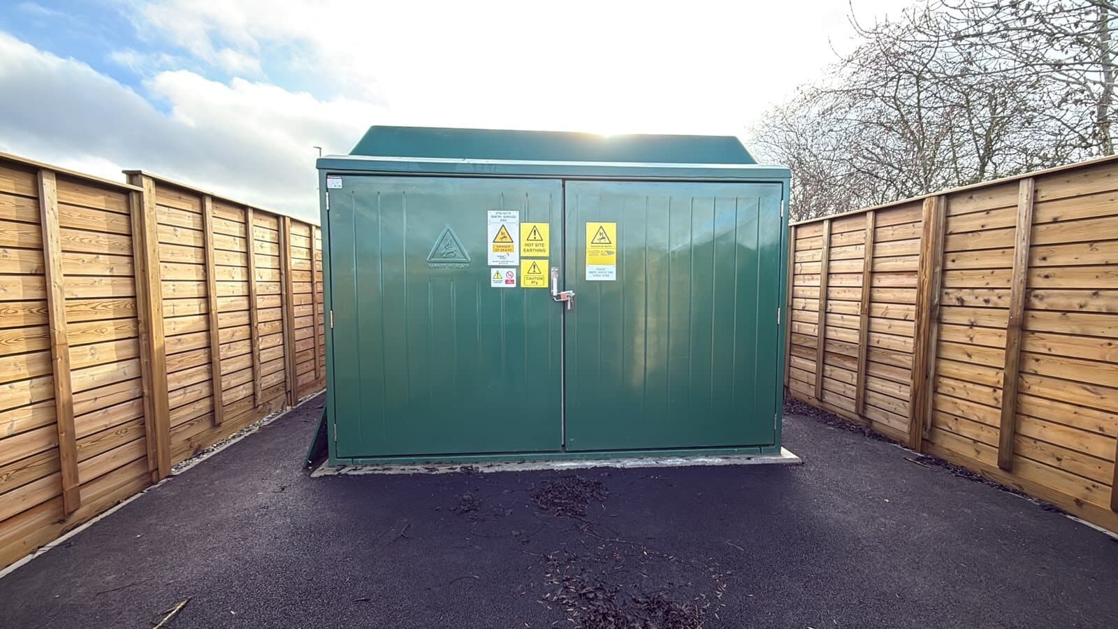 Substation kiosk finished inside a timber screen on new tarmac, with warning labels fitted